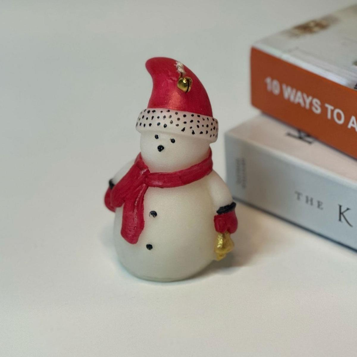 12 cm yüksekliğinde kokulu kardan adam figürlü mum. Kırmızı şapka ve atkısı olan, dekoratif yılbaşı mumu.