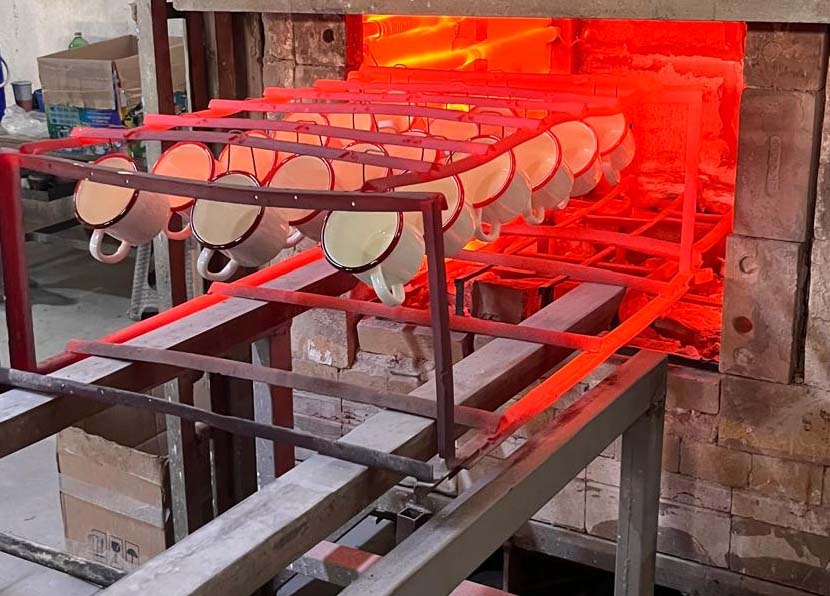 Yüksek sıcaklıktaki fırında emaye kaplama işlemi sırasında asılı duran beyaz emaye kupalar.