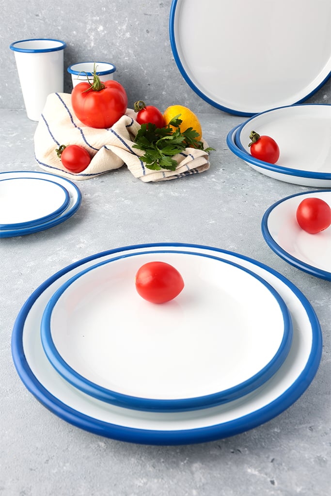Modern mutfak tezgahında taze domateslerle sergilenen, Emayeci'ye ait mavi kordonlu emaye tabak ve bardak seti, mutfakta sağlık ve hijyen vurgusu.
