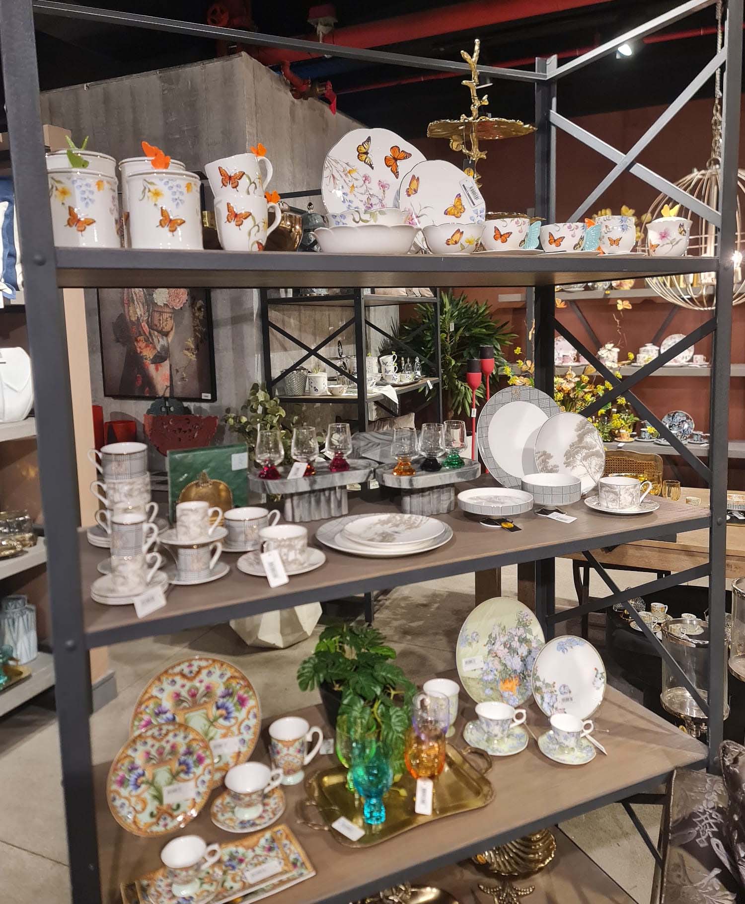 Mikasa Moor markasına ait kelebekli, floral ve geometrik desenli lüks kahve fincan takımları, yemek tabakları, servis setleri ve cam aksesuarların bulunduğu bütünsel sofra sunumu rafı