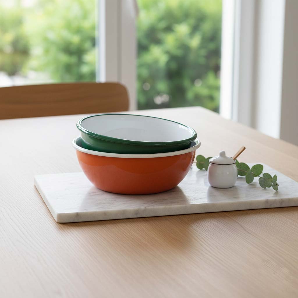 Modern bir sofrada, mermer servis tabağı üzerinde duran, kendinden kıvrımlı, yeşil ve turuncu renkli emaye kaseler ile şık ve minimalist bir sunum.