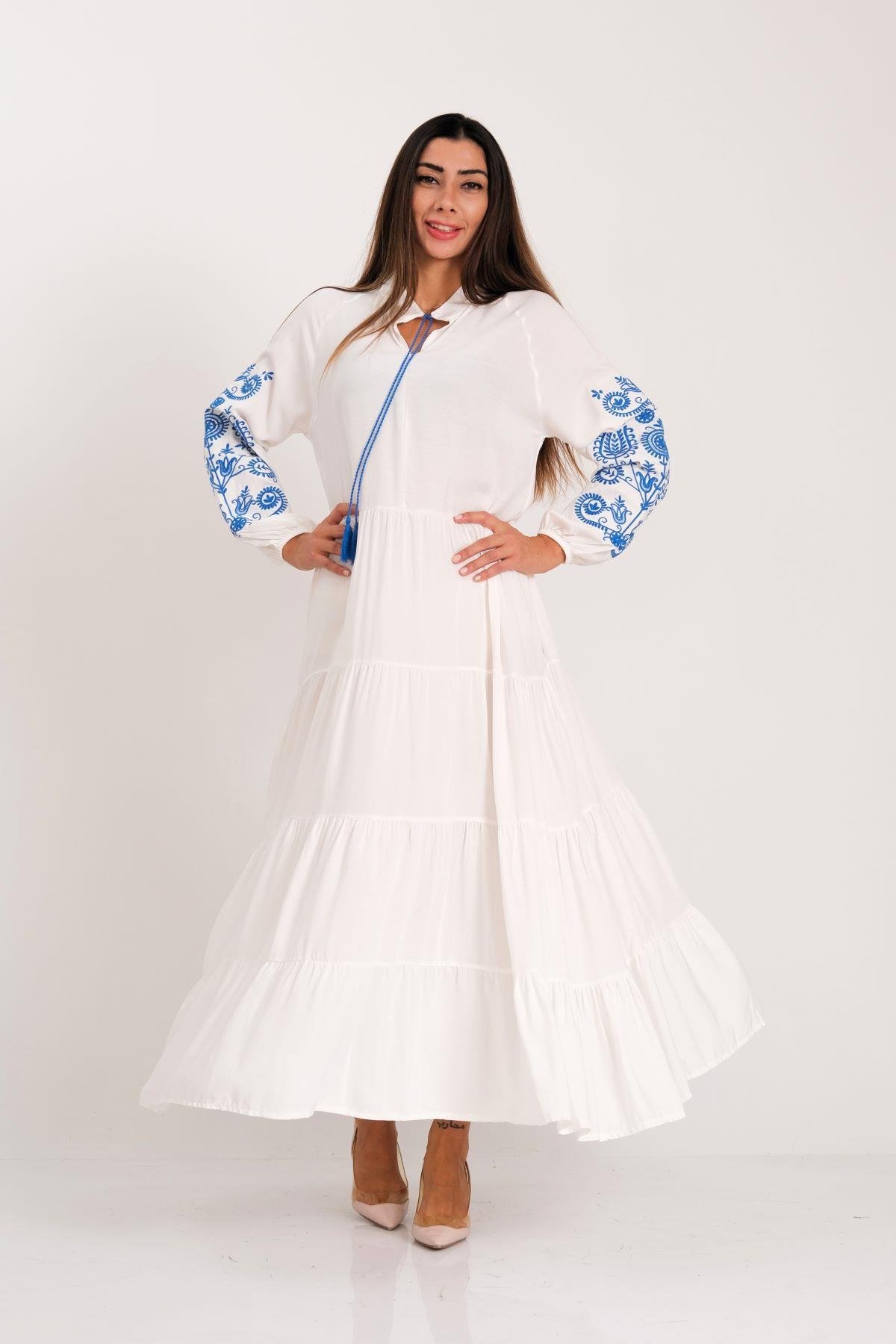 فستان أبيض أبيض بياقة صفرية وأكمام بأربطة شرابة وأربطة بأكمام مطرزة وتنورة طويلة ذات طبقات