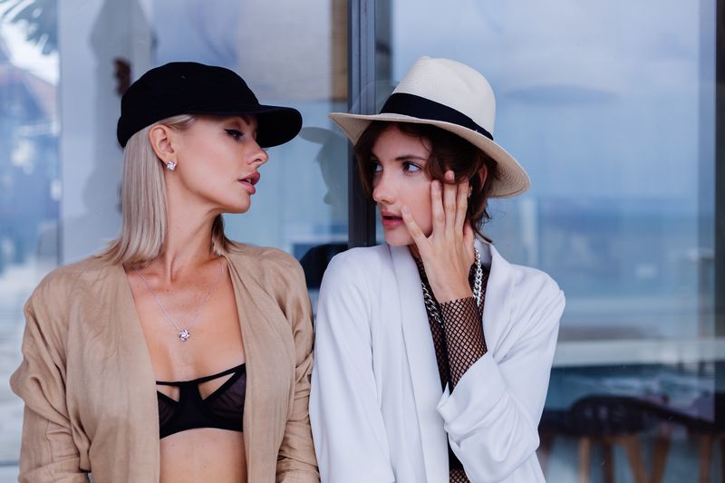 Blazer ceket giyen iki genç kadın şapka takmışlar birbirlerine bakıyorlar