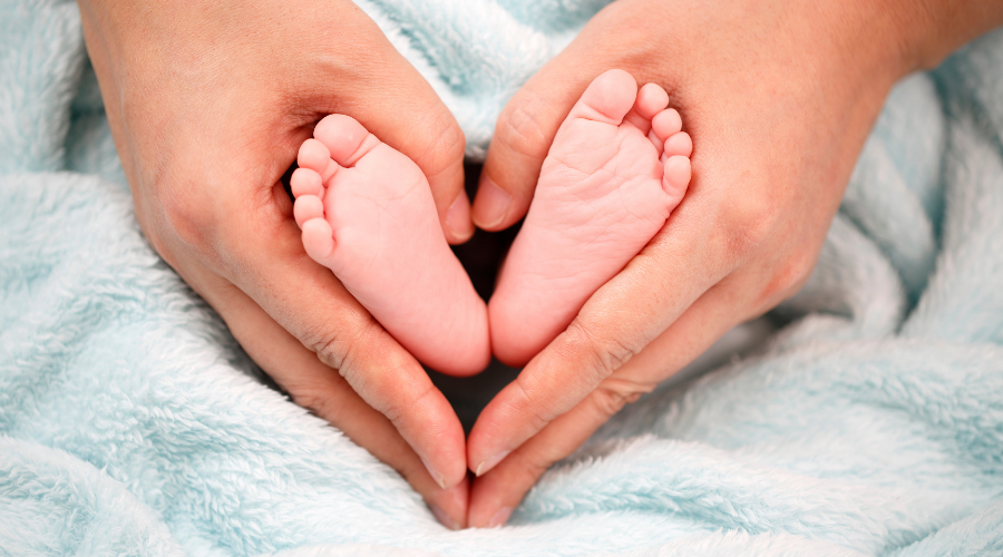 Yeni doğan bebeğin ayaklarını tutarak kalp yapan bir baba.