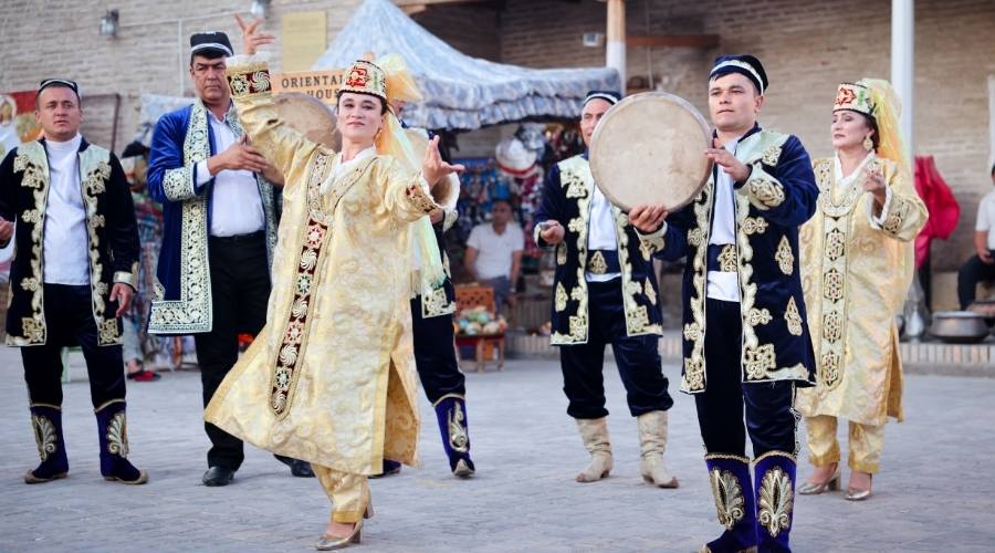 Umay isimli bir kadının arkasında ulusal kıyafetler giymiş bir şekilde dans eden özbek insanlar.