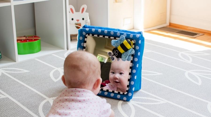 Tummy time nedir tummy time pozisyonunda mavi desenli aynasına bakan pembe kıyafetli tatlı kız bebek