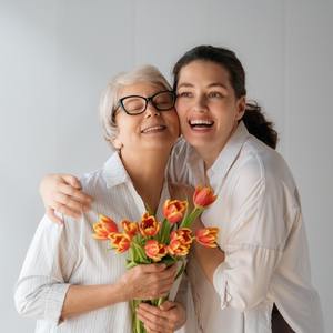 yaşlı ve gözlüklü annesine çiçek veren ve sarılarak gülen bir yetişkin