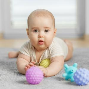 Bebek, halının üzerinde yatarken duyusal topu tutuyor. Karın üstü oyun zamanı.