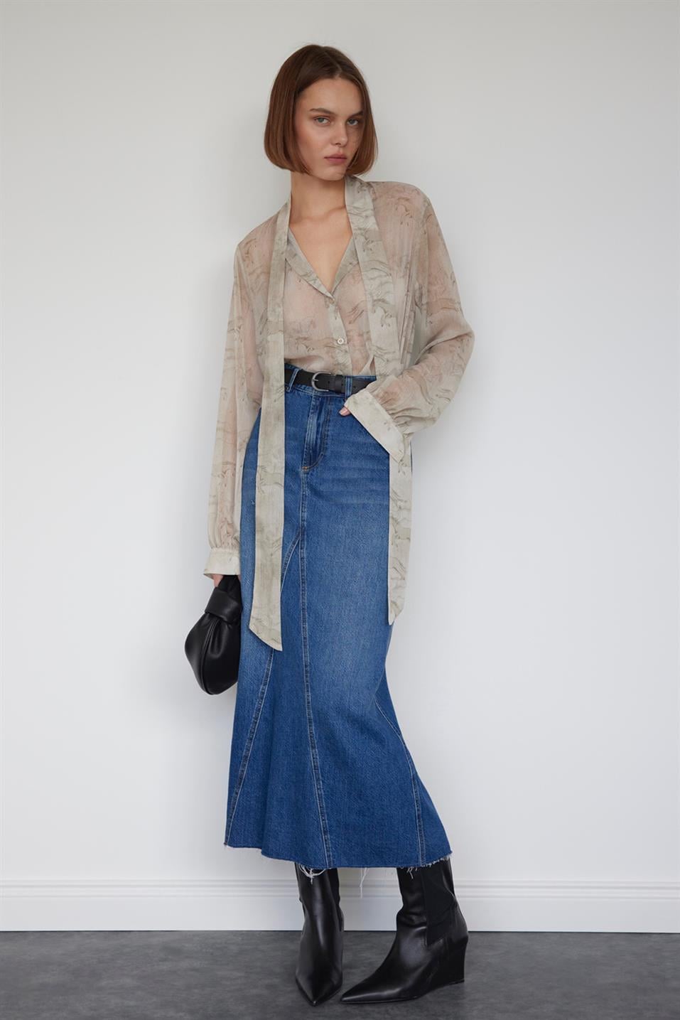 Stylish model in a denim skirt, paired with a flowing blouse and black boots, showcasing trendy denim skirt styles.