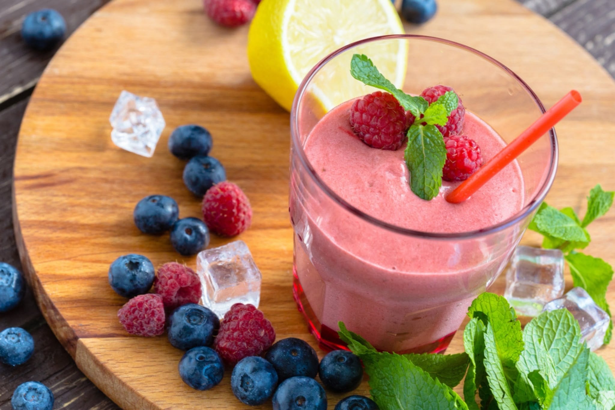 Ahşap masa üzerinde yaban mersini, böğürtlen, ahududu ve çilekle hazırlanmış mor renkli ev yapımı smoothie bardağı.