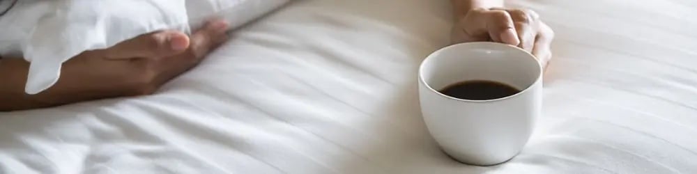 Kahvenin uyku üzerindeki etkisi için yatakta kahve fincanına uzanan el