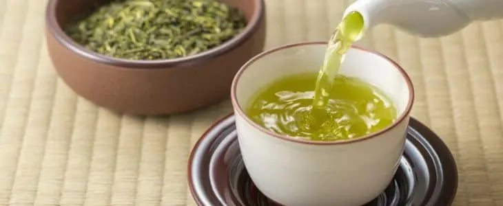 Yeşil çayın beyaz fincana dökülüşü ve kuru yeşil çay yaprakları