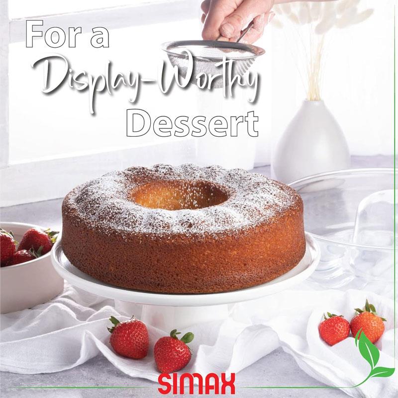 Simax cam fırın kabında pişirilmiş, üzerine pudra şekeri elenen halka kek (bundt cake). Kek, çileklerle süslenmiş bir servis tabağında sergileniyor. 'For a Display-Worthy Dessert' (Sergilenmeye Değer Bir Tatlı İçin) yazılı.