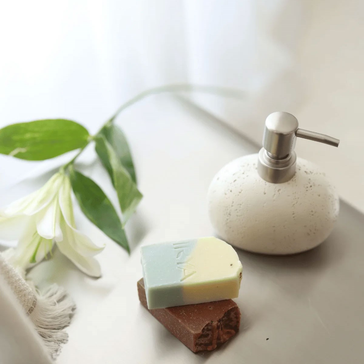 Beyaz tezgah üzerinde traverten dokulu sıvı sabunluk, bitkisel kalıp sabunlar ve beyaz zambak