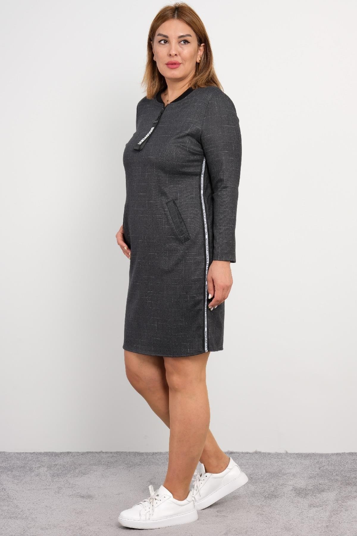  Bu elbise, koyu gri renkte, uzun kollu ve diz üstü uzunluğundadır. Ürünün ön kısmında bir fermuar detayı bulunur ve yanlarda beyaz şerit detayı vardır. Elbisenin bel hizasında iki adet cep bulunmaktadır. Arka kısmı düz ve sade bir tasarıma sahiptir.