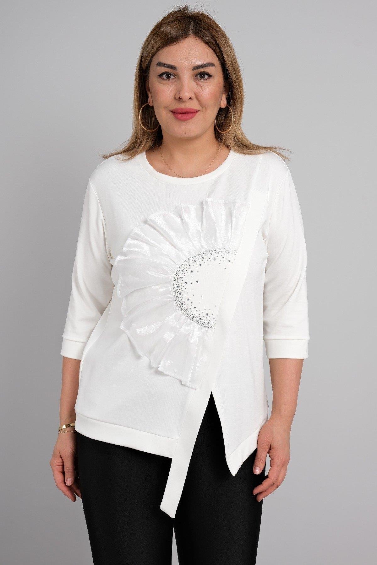  Bu görsellerde, beyaz renkte ve yarım kollu bir bluz bulunmaktadır. Ön kısmında dikkat çeken büyük bir çiçek deseni yer almakta olup, desenin merkezinde sim detayları bulunmaktadır. Bluzun etek kısmında hafif bir asimetrik kesim mevcuttur. Kumaşı ha