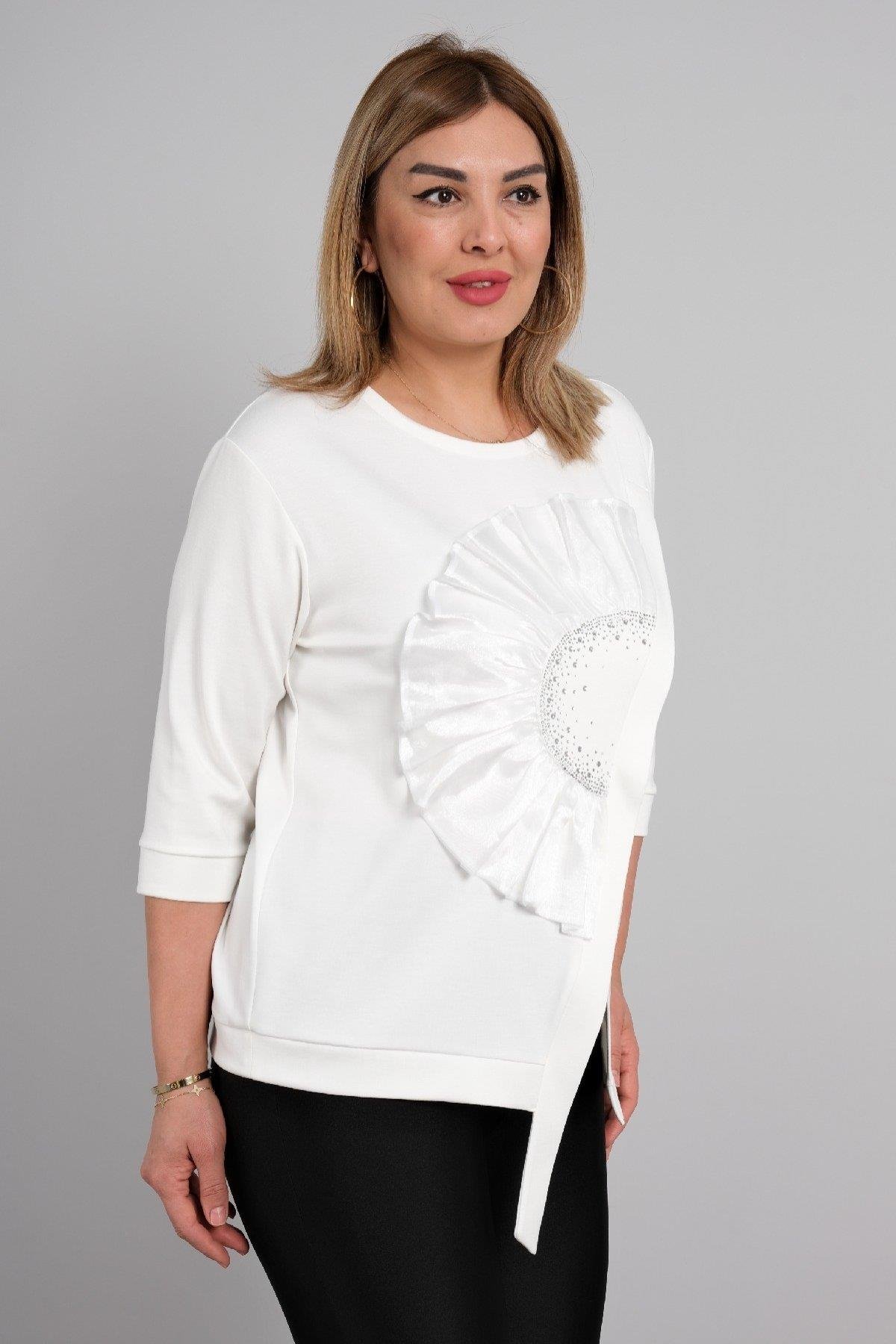  Bu görsellerde, beyaz renkte ve yarım kollu bir bluz bulunmaktadır. Ön kısmında dikkat çeken büyük bir çiçek deseni yer almakta olup, desenin merkezinde sim detayları bulunmaktadır. Bluzun etek kısmında hafif bir asimetrik kesim mevcuttur. Kumaşı ha