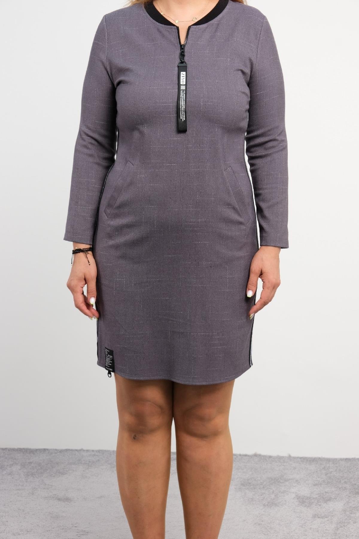  Model üzerinde görülen bu elbise koyu gri renkte ve spor bir tarza sahiptir. Elbise, uzun kollu olup, ön kısmında fermuarlı bir detay bulunmaktadır. Yandan bakıldığında, iki yan cep detayı barındırmaktadır. Elbisenin sol tarafında dikey bir şerit de