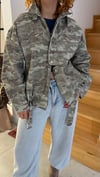 Kamuflaj desen, dik yaka ve metal detayları bir araya getiren ceket modeli.